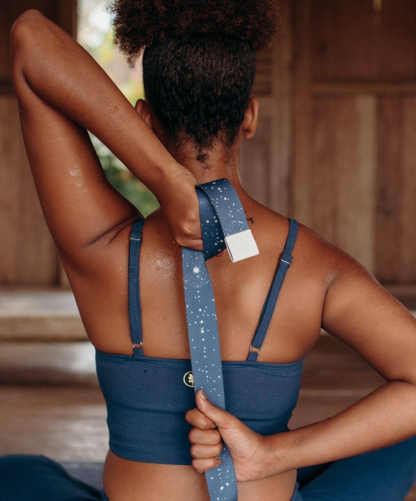 Person wearing a blue sports bra and holding a yoga strap with a wooden background