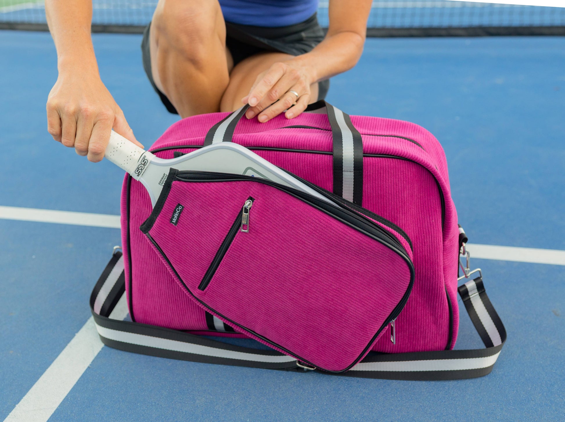 Person holding a pink duffel bag with a tennis racket on a blue court