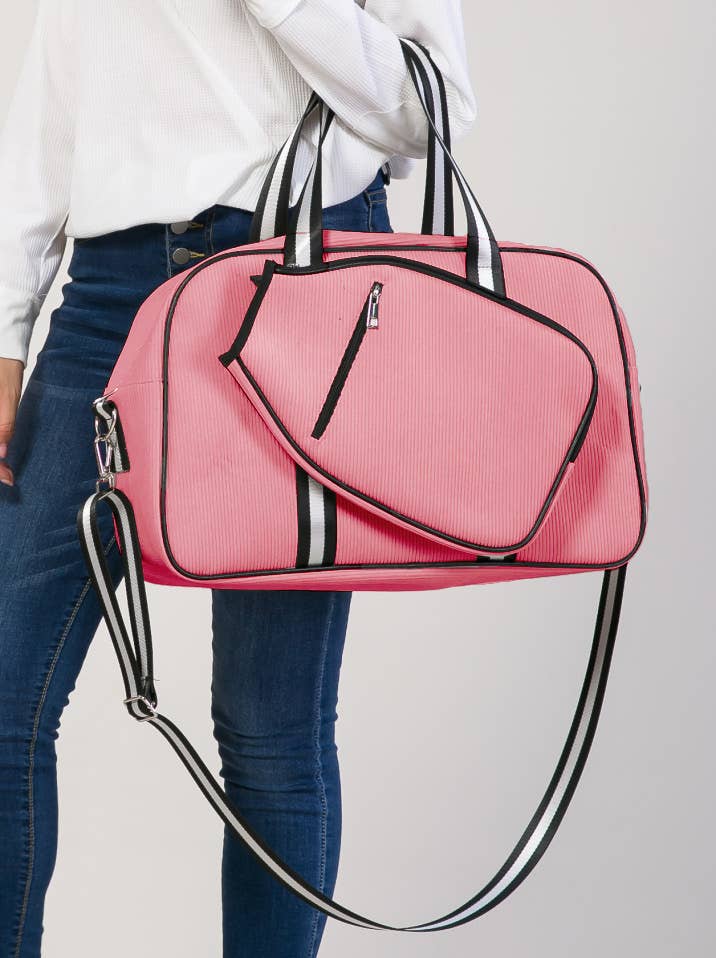 Pink duffel bag with black accents held by a person wearing a white sweater and blue jeans on a light gray background.