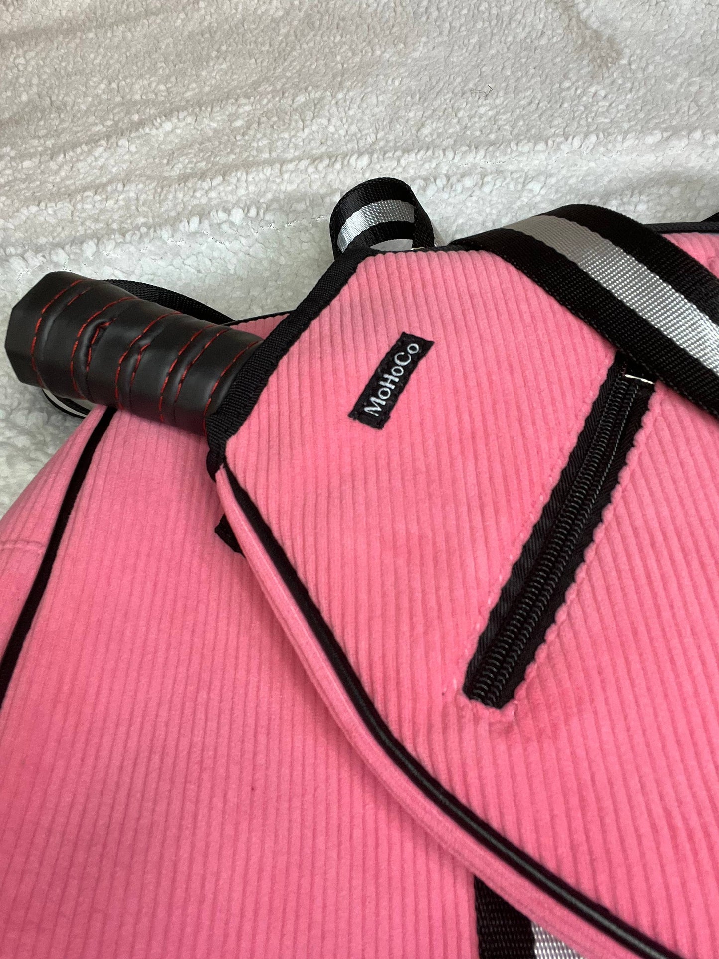 Pink dog coat with black trim and a visible brand label on a textured surface.