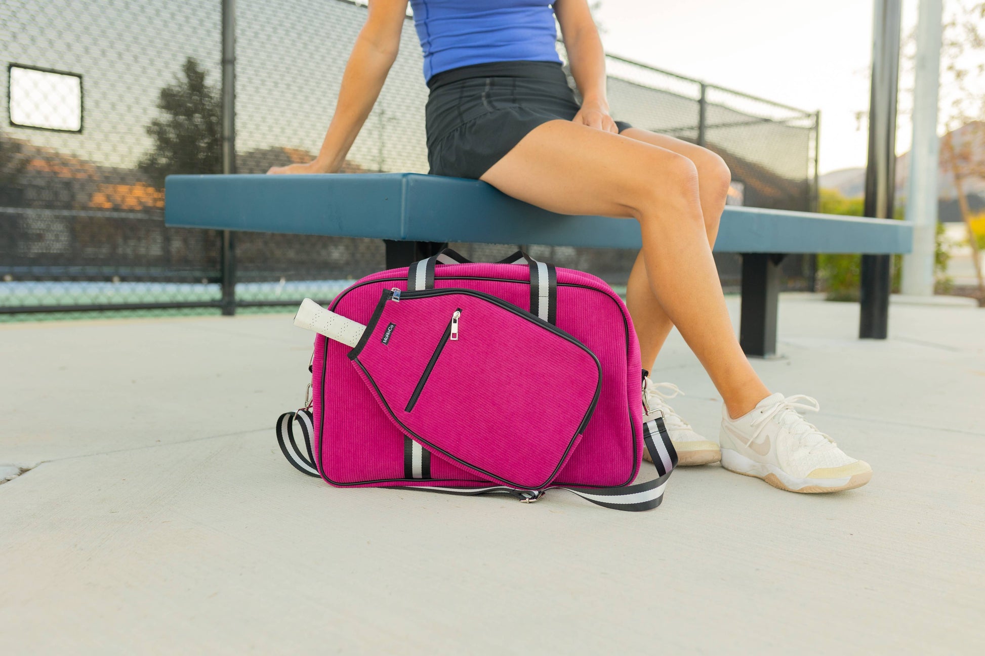 Person sitting on a bench with a pink suitcase in front of them, outdoors.