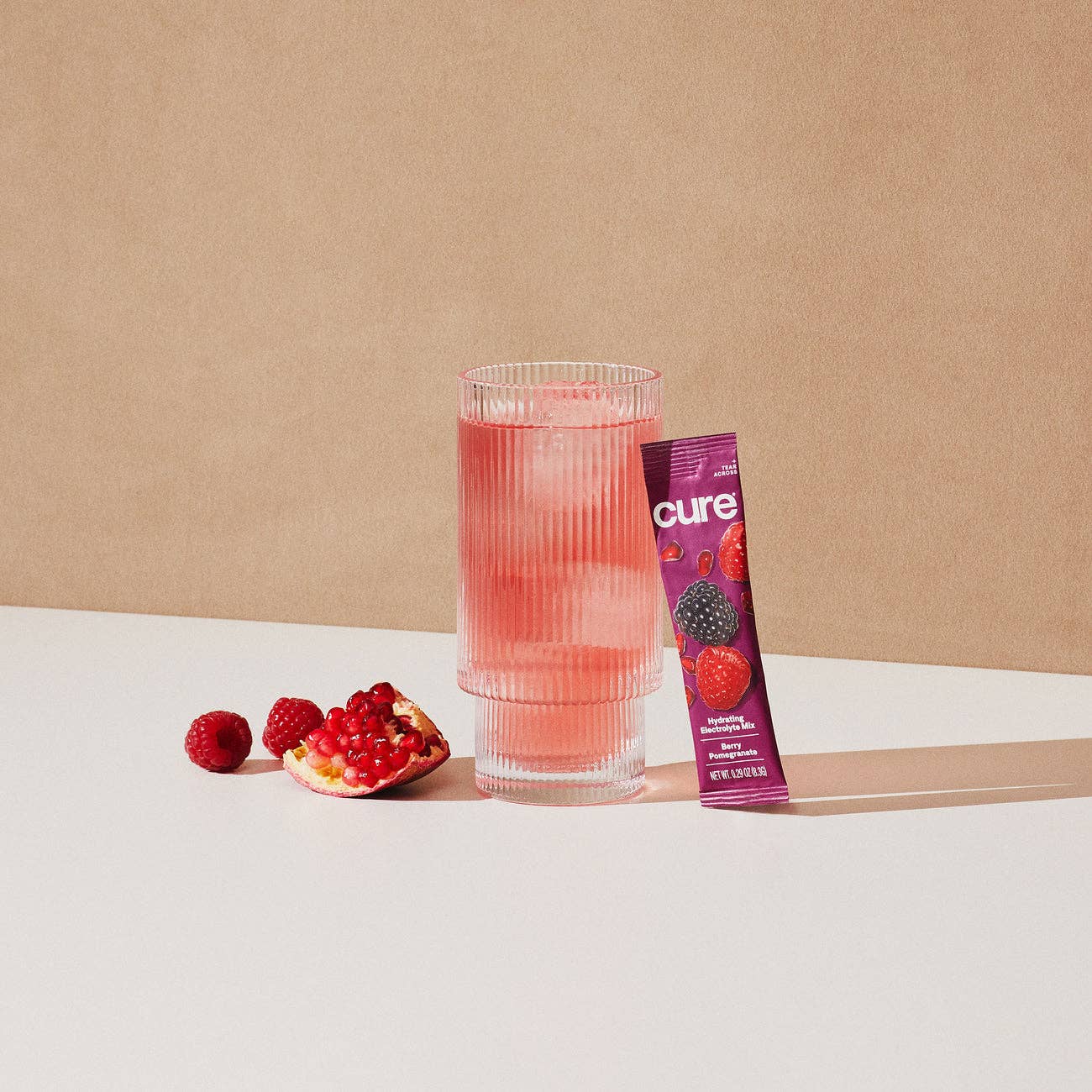 Glass of pink drink with raspberries and a 'cure' package on a beige background